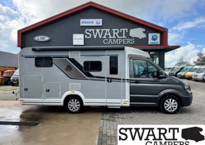 Grey and white motorhome parked in front of Swart Campers dealership with signage logos in the background.