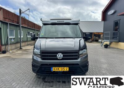 Front view of a gray VW camper van with a raised KNAUS roof, yellow Dutch license plate KHK-05-Z, parked on a paved lot.