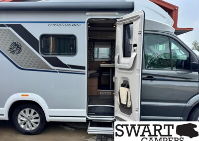 Grey and white camper van with the side door open, revealing the interior living area and seating near the entry.