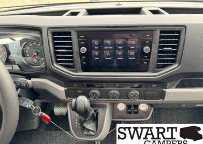 Car dashboard interior featuring a central touchscreen, air vents, climate controls, an automatic gear shifter, and keys in the ignition; SWART CAMPERS watermark visible.