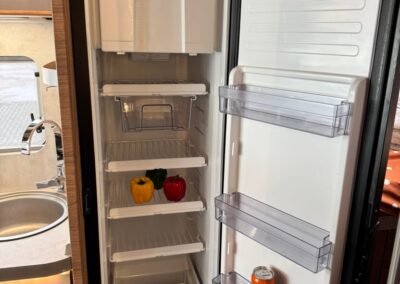 Open compact refrigerator in a camper with two bell peppers on the middle shelf and a can on the door rack.