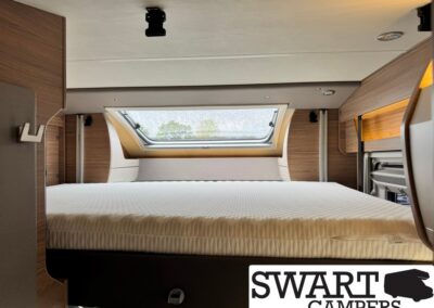 Camper van bedroom with a low platform bed, white mattress, wood paneling, and a skylight window.
