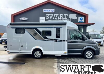 Side view of a gray and white motorhome parked in front of a Swart Campers dealership.