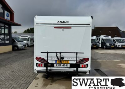 Rear view of a white KNAUS caravan with a black bicycle rack, license plate KHF-41-R, parked among other campers.