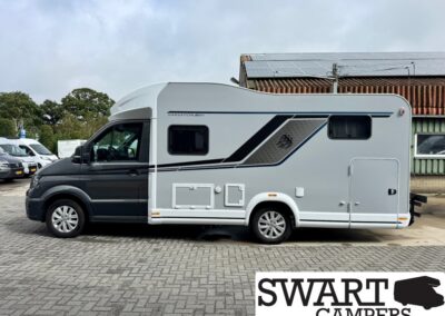 Side view of a white and gray motorhome with solar panels on the roof, parked on a paved lot.