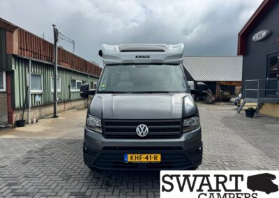 Front view of a gray VW camper van with a raised KNAUS pop-up roof, parked in an industrial yard; SWART CAMPERS logo bottom right.