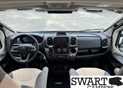 Front cabin of a Fiat camper van with steering wheel, central touchscreen, gear shifter, and beige seats.