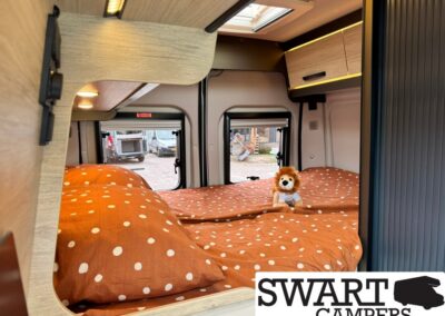 Camper van bedroom with orange polka-dot bedding and a small lion plush on the bed by the window.