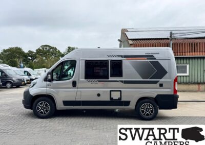 Side view of a silver camper van with roof solar panels and geometric gray decals, parked outdoors.