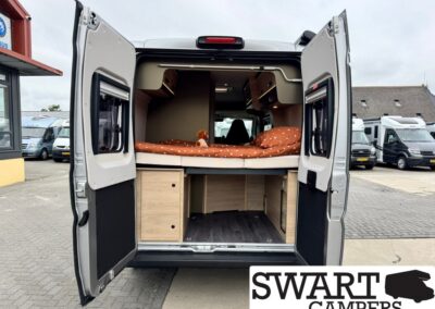 Rear view of a camper van with the bed raised above built-in wooden cabinets and storage under it