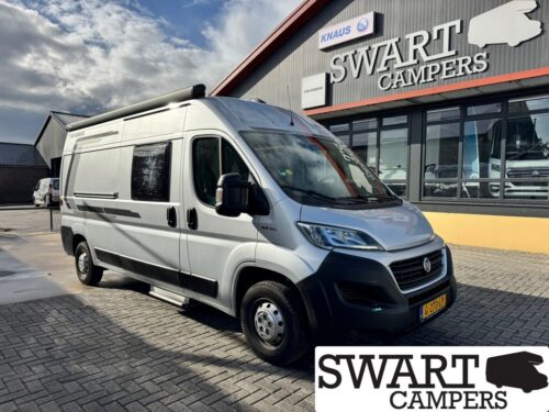 Silver camper van parked outside a Swart Campers showroom, with a large Swart Campers sign on the building nearby.