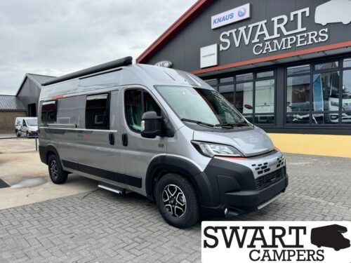 Silver camper van parked in front of a SWART CAMPERS storefront, showing a black bumper and side steps under a cloudy sky.