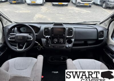 Inside view of a Fiat camper van cockpit: steering wheel on the left, central touchscreen, climate controls, gear lever, two front seats, and a SWART CAMPERS logo overlay in the bottom right.
