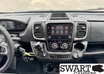 Center dashboard of a van with a touchscreen infotainment screen, climate dials, gear shifter, and steering wheel.