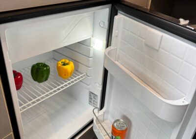 Open compact camper fridge with three bell peppers (red, green, yellow) on the shelf and a can in the door pocket.