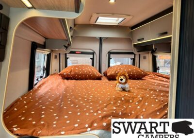Interior of a campervan bedroom with a large orange polka-dot bed, two pillows, and a small plush lion by the center.