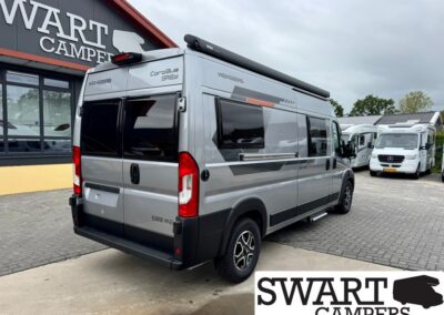 Silver camper van with dark windows and a roof awning parked outside a dealership (Swart Campers).