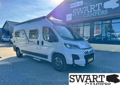 White camper van parked outside a Swart Campers showroom, with the building’s SWART CAMPERS sign visible above.
