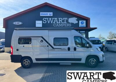 Side view of a white camper van with black decal parked in front of a Swart Campers building with logos and signage above.