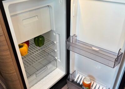 Open compact camper fridge with peppers on the lower shelf and a canned drink in the door bin; freezer compartment visible at the top.