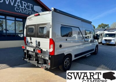 White KNAUS BoxLife camper van with a rear bicycle rack parked outside the Swart Campers showroom, showing its rear doors and windows.