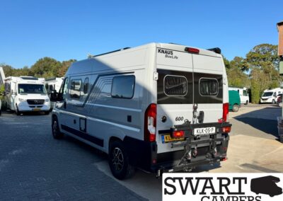 Rear three-quarter view of a white Knaus BoxLife camper van with a bike rack at the back, parked in a lot with other motorhomes; SWART CAMPERS watermark in the corner.
