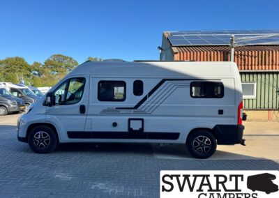 White camper van with black decorative stripes, parked on a paved lot under a clear blue sky; solar panels are mounted on the roof.