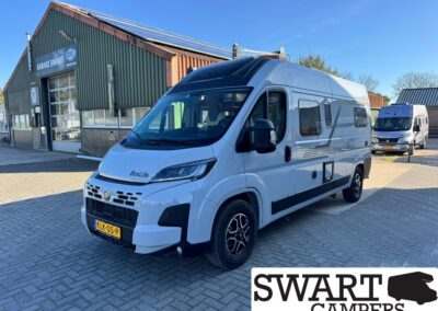 White BoxLife camper van parked outside a workshop labeled Swart Campers, with another van in the background and a clear blue sky.