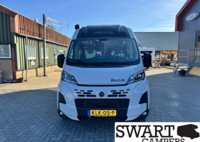 Front view of a white BoxLife camper van parked in a paved lot with a clear blue sky behind it (Dutch license plate KLK-05-P).