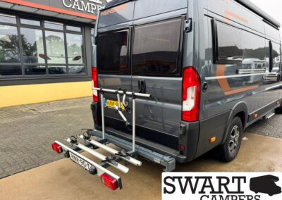 Grey camper van with a rear bike rack mounted on the back, parked outside Swart Campers; license plate HNR-90-T.