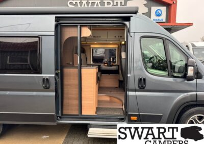 Grey camper van with side door open, revealing a wooden kitchenette and seating area inside.