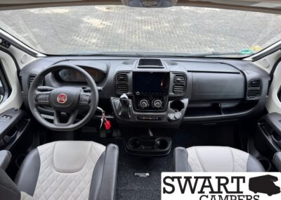 Front cab of a camper van with a Fiat steering wheel, central touchscreen, gear shifter, and two captain chairs; SWART CAMPERS watermark.
