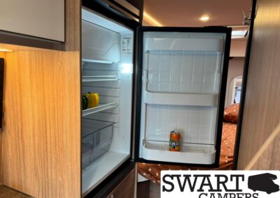 Open compact RV fridge with peppers on the middle shelf and a single can of Fanta in the door shelf.
