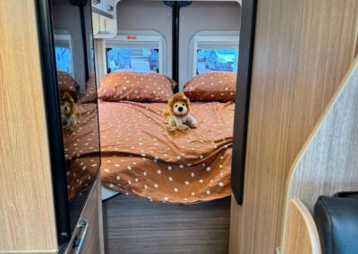 Interior of a caravan bedroom with a brown polka-dot duvet, a small stuffed lion on the bed, and mirrored wardrobes along the sides under a skylight.