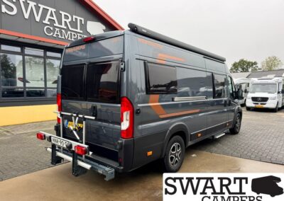 Gray camper van with orange accent stripes parked outside a showroom that reads SWART CAMPERS, with a rear bike rack and Dutch license plate HNR-90-TX.