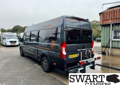 Rear view of a dark gray camper van with orange graphics and a bike rack, Dutch license plate visible in a parking lot.