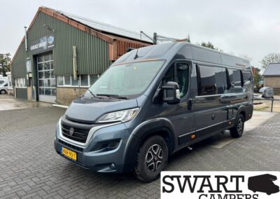 Grey camper van parked outside a workshop building with a sign reading Garage Swart in the background