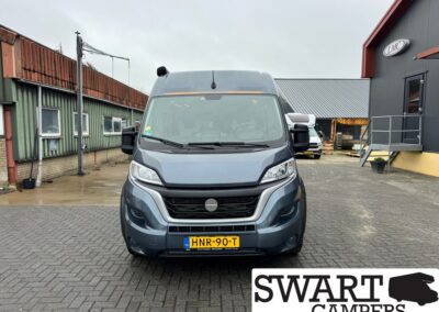 Front view of a gray-blue camper van in a paved yard, license plate HNR-90-T, SWART CAMPERS logo bottom right.